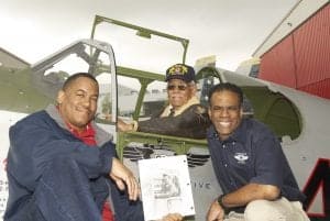Craig Huntly holds a picture of his uncle, Clarence E. Huntley, Jr. showing him sitting in the cockpit of Skipper’s Darlin’ III as a 19-year-old crew chief. Clarence recreated that picture by sitting in the cockpit of the CAF Red Tail Project’s Mustang Tuskegee Airmen. Project Leader and Mustang pilot Brad Lang in on the right. (photo courtesy of Bruce Talamon)